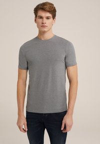 Camiseta de manga corta y cuello redondo en tejido de algodón gris claro. Diseño simple, textura suave y forma ajustada, combinada con jeans oscuros.