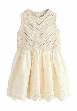 Sleeveless cream baby dress with knitted bodice, scalloped edges, and eyelet-embroidered gathered skirt.