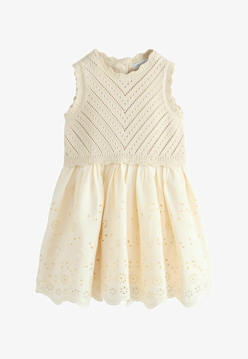 Robe bébé crème sans manches avec corsage tricoté, bords festonnés et jupe froncée brodée d'œillets.
