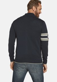 Dunkelblauer Strickcardigan mit Schalkragen, der einen grauen Streifen und ein Logo-Patch auf dem linken Ärmel aufweist. Mit gerippten Bündchen und Saum.