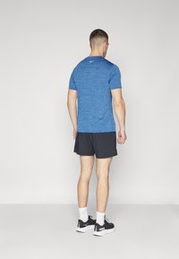 Blaues Sport-T-Shirt mit kurzen Ärmeln, strukturiertem Stoff, kombiniert mit schwarzen Shorts und schwarzen Sportschuhen mit weißen Sohlen.