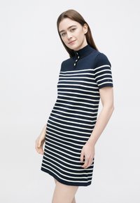 Polo-Kleid mit marineblauen und weißen Streifen, kurzen Ärmeln, Kragen und goldfarbenen Knöpfen. Weicher Strickstoff; figurbetonte Passform mit geradem Schnitt.