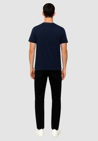 T-shirt in cotone blu navy con collo rotondo, maniche corte e vestibilità regolare, abbinato a pantaloni neri e sneakers bianche. Design semplice.