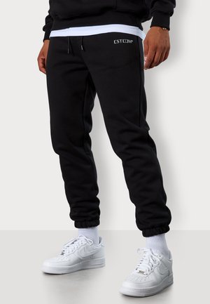 Black sweatpants with an elastic waistband and cuffs, featuring a subtle "ESTEEM" logo. Paired with white sneakers and white socks.