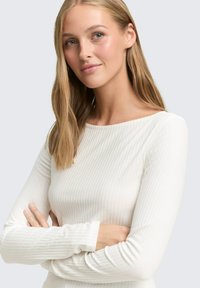 Langsleeve geribbelde top van zachte witte stof, met een bootnecklijn en een getailleerd ontwerp. Glad textuur met subtiele verticale strepen.