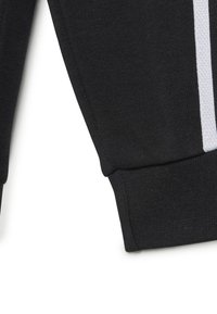 Tessuto in felpa nero con texture a coste, caratterizzato da un dettaglio a striscia bianca lungo la manica e un polsino aderente nella parte inferiore.