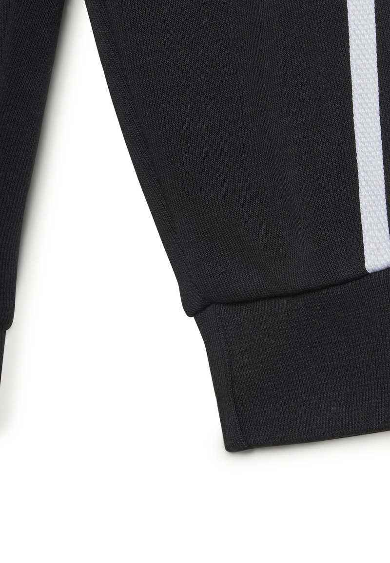 Tessuto in felpa nero con texture a coste, caratterizzato da un dettaglio a striscia bianca lungo la manica e un polsino aderente nella parte inferiore.