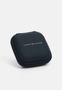 Custodia nera con zip caratterizzata dal logo in rilievo "TOMMY HILFIGER". Forma a quadrato arrotondato con texture liscia e accento di colore contrastante nel logo.