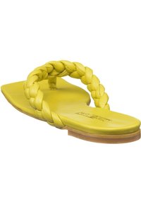 Sandale plate en cuir jaune avec un design de bride tressée, possédant une texture lisse et une forme moderne minimaliste. Détail de semelle marron.