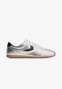 Stříbrná sportovní obuv s hladkým povrchem, černými akcenty, bílými tkaničkami a světle hnědou podrážkou. Disponuje elegantním, minimalistickým designem.