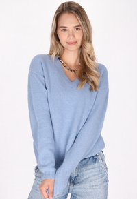 Pulover bleu deschis cu guler în V, realizat dintr-un material tricotat moale și texturat; ajustat confortabil, cu mâneci lungi. Asortat cu blugi din denim deschis.