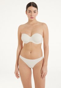 Beżowy biustonosz bez ramiączek z formowanymi miseczkami i gładką teksturą, zestawiony z pasującymi majtkami w stylu bikini o minimalnym kroju i bezszwowych brzegach.