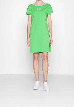 Green cotton t-shirt dress with short sleeves and a scoop neckline, featuring a white logo on the front. Worn with white sneakers.