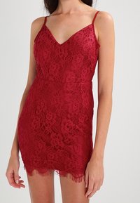 Robe mini en dentelle rouge avec un décolleté en V, des bretelles spaghetti réglables, un motif floral et un ourlet festonné. Présente une silhouette cintrée et une texture douce.
