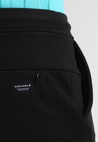 Pantalons de survêtement noirs avec une poche zippée, texture douce, taille élastique et une étiquette de marque avec le logo "BJÖRN BORG".