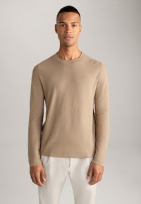 Chemise beige à manches longues texturée avec un col rond, accompagnée de pantalons de couleur claire. Tissu lisse et coupe ajustée pour un look moderne.