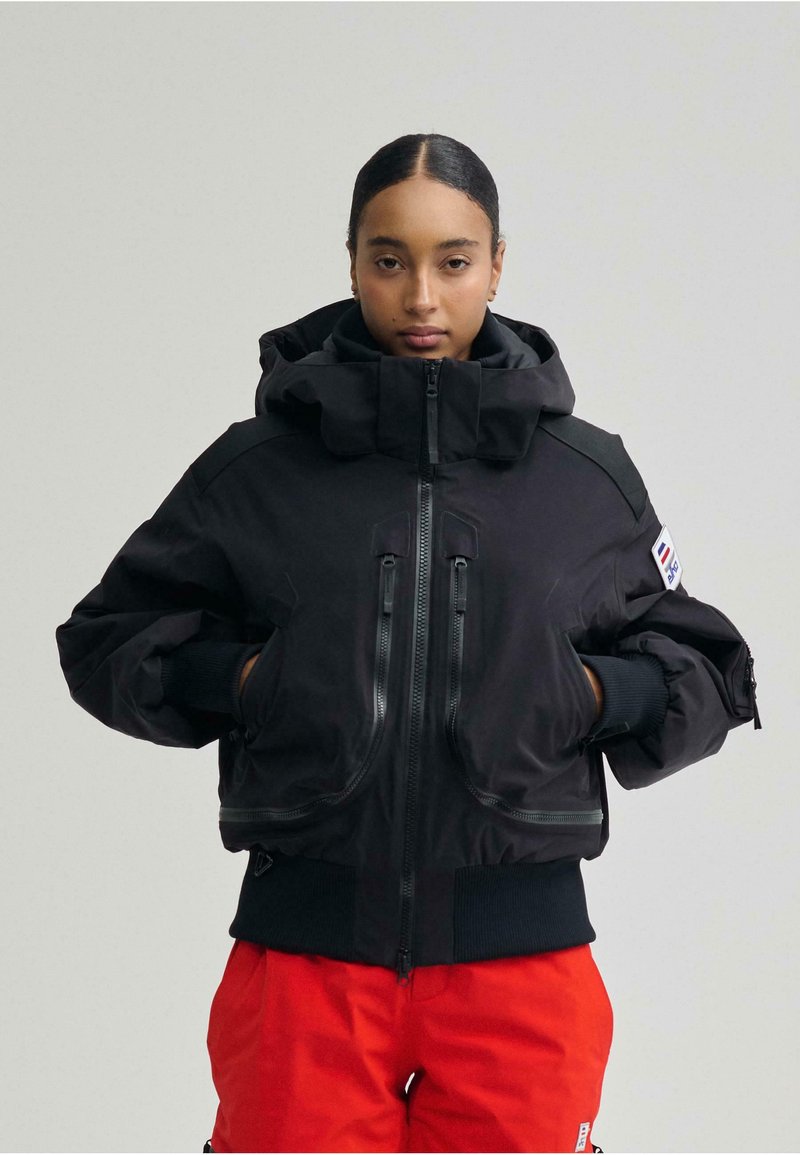 Fekete pufi kabát magas gallérral, cipzáras elejű és két mellzsebbel. Texturált anyagból készült, bordázott ujjvégekkel.