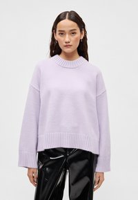 Λιλά πλεκτό πουλόβερ με ριμπ γιακά και μανσέτες, με άνετη εφαρμογή και υφή υφάσματος. Συνδυάζεται με γυαλιστερά μαύρα παντελόνια.