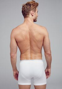 Calzoncillos de algodón blancos con un ajuste ceñido y cinturilla elástica, vistos desde atrás, mostrando una textura suave y un diseño simple.