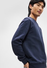 Sweatshirt azul marinho feito de tecido texturizado, com decote redondo, punhos e bainha canelados, com design minimalista e sem logótipos visíveis.