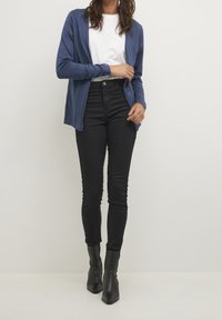 Marineblauer Langarm-Cardigan aus leichtem Stoff, kombiniert mit einem weißen T-Shirt und hochtaillierten schwarzen Skinny-Jeans. Schwarze Stiefeletten.