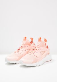 Světle růžové sportovní boty s mřížkovou vrchní částí, šněrováním a bílou gumovou podrážkou. Obsahují dvojité poutka a logo na jazyku.