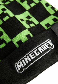 Schwarze Strickmütze mit pixeliertem grünen Creeper-Design. Weißes, gesticktes "Minecraft"-Logo am Saum, strukturiert für Wärme.