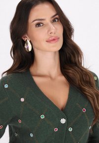 Cardigan verde din lână cu decolteu adânc în V, decorat cu bijuterii colorate și un model cu diamante. Are mâneci lungi și tricot texturat.