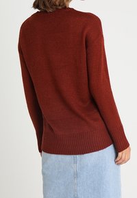 Sweter z dzianiny w kolorze rdzy z prążkowanymi mankietami i dołem, o luźnym kroju i fakturowanym wzorze, zestawiony z jasnoniebieską jeansową spódnicą.