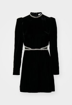 Mustapuku, jossa on pitkät hihat, korkea kaulus ja hopeaketjuvyö. Ominaisuuksiin kuuluu muotoiltu yläosa ja liehuva hame, sileä pinta ja hillitty kiilto.