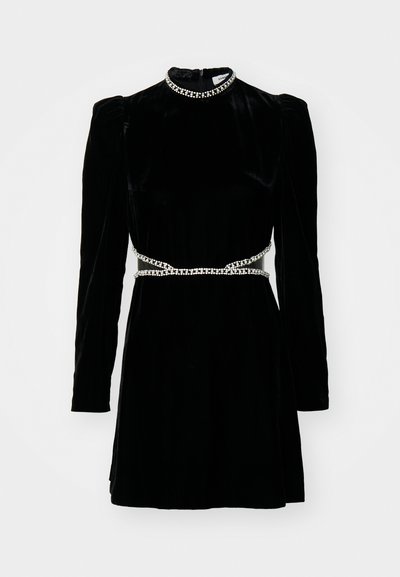 Robe en velours noir avec des manches longues, un col haut et une ceinture en chaîne argentée. Elle présente un corsage ajusté et une jupe évasée, une texture lisse et un léger éclat.