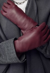 Burgundy leather gloves with a smooth texture, featuring three outlined fingers, positioned over a dark gray coat with a herringbone pattern.
