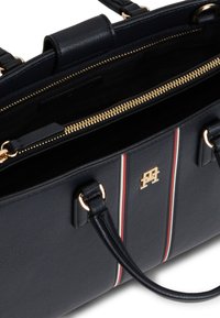 Τσάντα ώμου από δέρμα σε ναυτικό μπλε με διπλές λαβές, χρυστό φερμουάρ, μικρό χρυσό λογότυπο και κάθετες ρίγες σε κόκκινο, λευκό και ναυτικό μπλε στο εμπρόσθιο πάνελ.