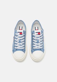 Blå canvas sneakers med vita gummisåler, med vita snören och en logotyp på tungan. Klassisk rund tådesign.