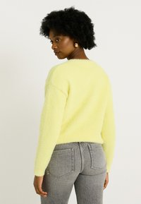 Pull moelleux de couleur jaune clair avec manches longues et décolleté arrondi, associé à un jean gris affichant deux poches arrière.