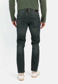 Donker denim jeans met een slim fit, voorzien van twee achterzakken en een nette afwerking. Gecombineerd met witte sneakers voor een casual uitstraling.