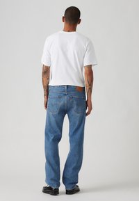 Blue denim jeans with a straight-leg fit, featuring back pockets and a leather patch on the waistband, paired with a white T-shirt.