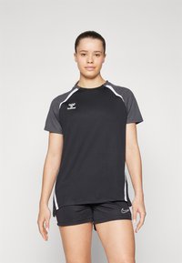 Svart treningstrøye med grå skulderpaneler, hvite detaljer og logo på brystet. Kombinert med svarte shorts med logo.