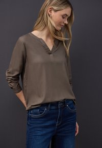 Brun, let blouse med V-hals og trekvart ærmer, parret med mørkeblå jeans. Glat tekstur med en afslappet pasform.