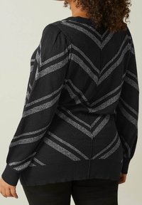 Pull noir avec un motif chevrons texturé en argent. Doté de manches bouffantes et d'un ourlet côtelé, fabriqué dans un matériau doux et scintillant.