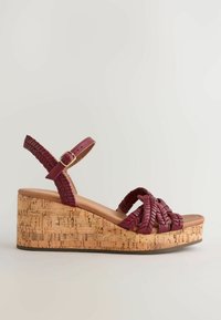 Sandale compensée avec plateforme en liège et brides tressées rouge foncé, dotée d'une boucle réglable à la cheville.