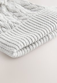 Lysegrå strikket hue med kabelmønster og ribbet kant. Materialet virker blødt med en chunky tekstur.