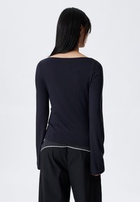 Tmavomodrá košeľa s dlhými rukávmi, štvorcovým výstrihom a priliehavým strihom. Mäkká, elastická látka, doplnená voľnými čiernymi nohavicami s bielymi detailmi.