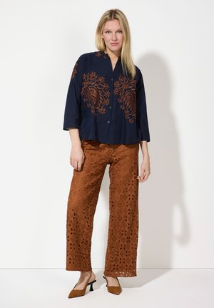 Navy blue shirt with orange floral embroidery and three-quarter sleeves paired with light brown lace trousers featuring intricate patterns.