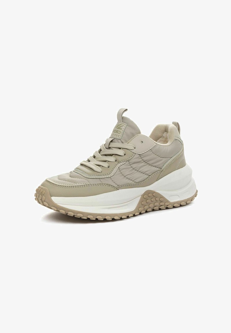 Beige sneaker met een gestructureerde bovenkant, een gevoerde tong en een rubberen zool met ronde noppen. Kenmerkt zich door contrasterende gladde en gestikte delen.