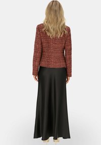 Czerwona marynarka z tweedu o strukturalnym fasonie, zestawiona z czarną satynową maxi spódnicą. Marynarka ma teksturowany materiał i dopasowany krój.