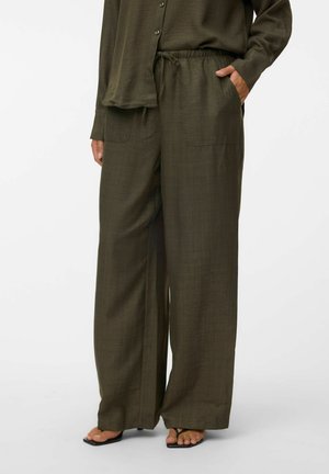 Femme portant un pantalon ample vert olive avec poches avant et une chemise boutonnée assortie, associée à des sandales noires à brides.