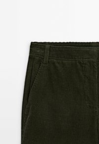 Pantalon en velours côtelé vert foncé avec passants pour ceinture et une poche latérale, montrant une texture côtelée verticale détaillée sur fond blanc.
