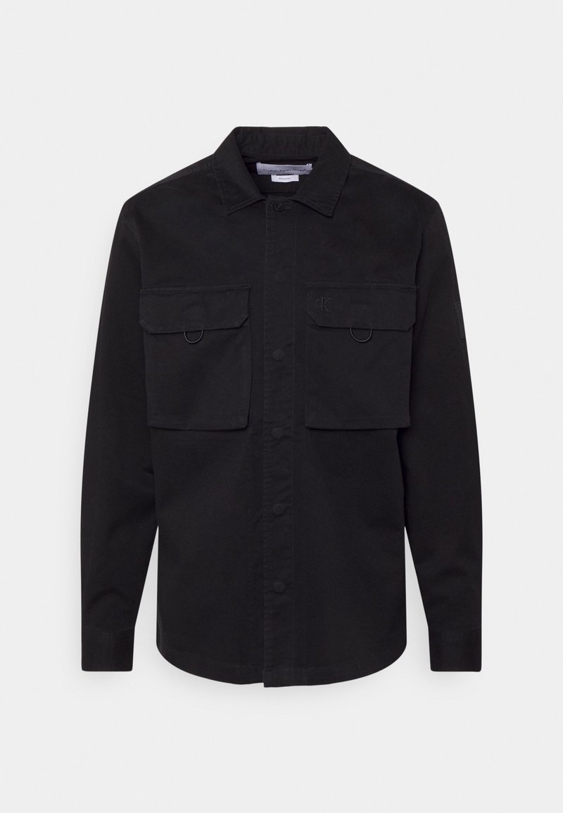 Svart långärmad skjorta i bomull med knappstängning fram, två bröstfickor och cirkulära detaljer. Har en krage.