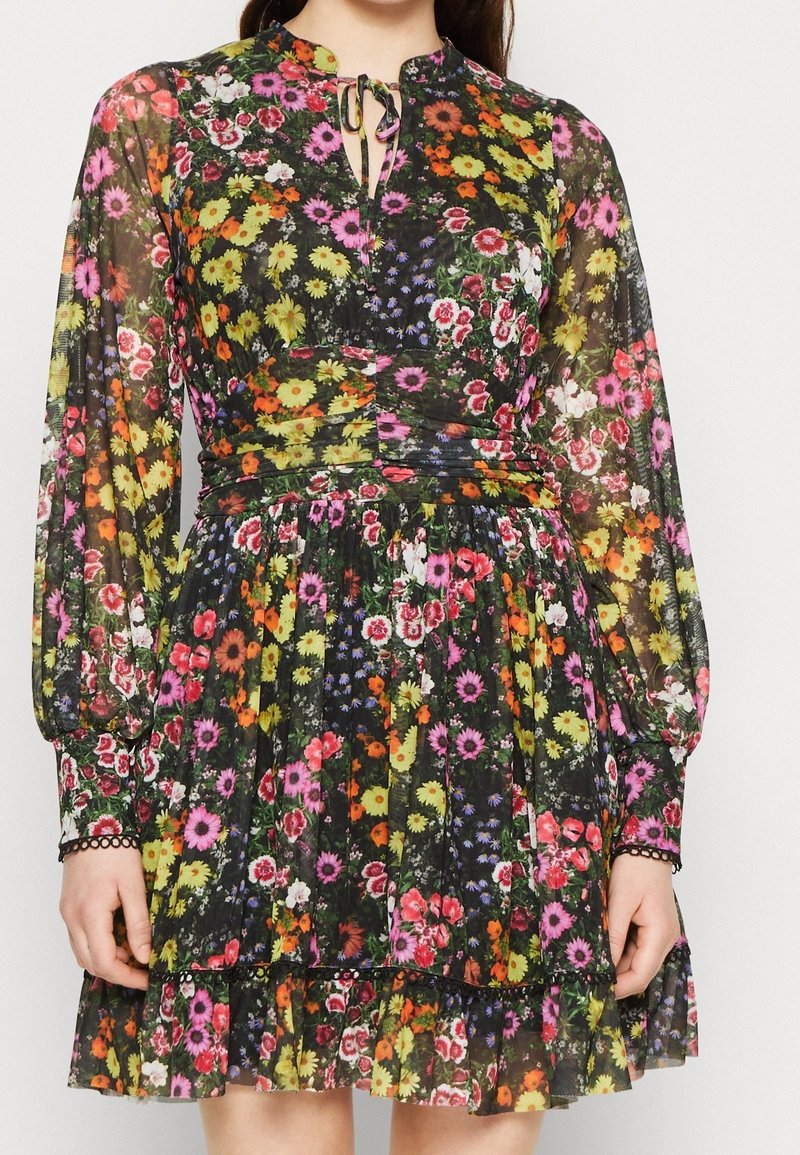 Robe fleurie avec un tissu noir transparent, un motif floral coloré, des manches longues, un décolleté en forme de trou de serrure et un ourlet à volants.